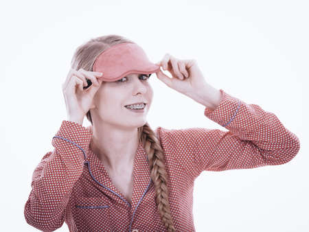 Sleep bedroom accessories concept. Happy sleepy woman wearing pink eye band and pajamas.の写真素材