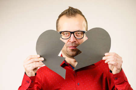 Depression, sadness, relationship problem concept. Man with broken heart full of negative sad emotions. Adult male holding two black halves of love symbol, on greyの写真素材