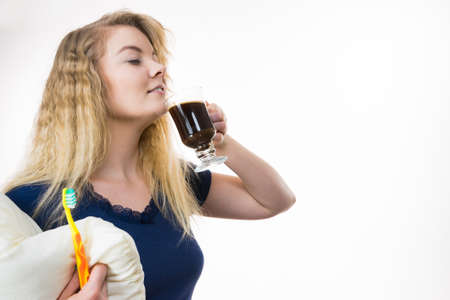 Funny woman holding black coffee and toothbrush being late. Getting morning energy, hurry up before going to work.の写真素材
