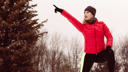 Outdoor sport exercises, sporty outfit ideas. Woman wearing warm sportswear pointing at copy space outside during winter.の写真素材