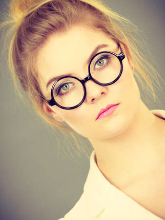 Bored focused or grumpy blonde college teacher or office orker woman wearing nerdy eyeglasses, white jacket.の写真素材