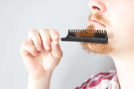 Bearded man having trouble with combing his beard using comb brush. Facial hair concept.の写真素材