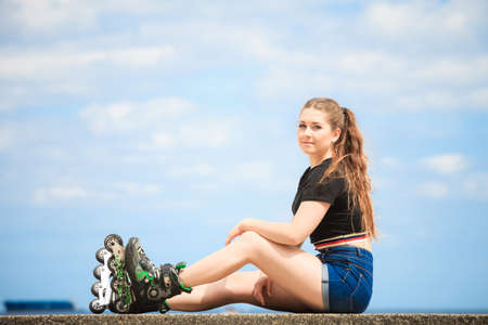 Happy joyful young woman wearing roller skates relaxing after long ride. Female being sporty having fun during summer time near sea.の写真素材