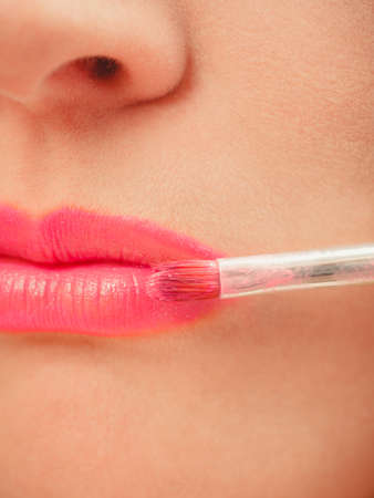 Close up of woman applying lipstick with brush on lips. Girl beautifying herself. Beauty and make up concept.の写真素材