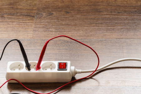 Measurement of voltage in electrical socket extension cord with multimeter on wooden floor backgroundの写真素材