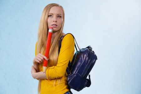 Smart young woman going to school or college wearing backpack and holding big pencil thinking about studyingの写真素材