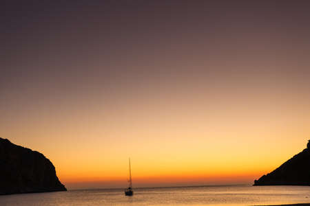Scenic sunrise or sunset over sea surface, yacht boat anchored in bay, Greeceの写真素材