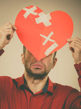 Bad relationships, breaking up, sadness emotions concept. Adult man holding broken heart, covering his face, on greyの写真素材
