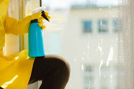 Female hand in yellow gloves cleaning window with blue rag and spray detergent. Spring cleanup, housework conceptの写真素材