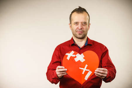 Bad relationships, breaking up, sadness emotions concept. Adult man holding broken heart, on greyの写真素材