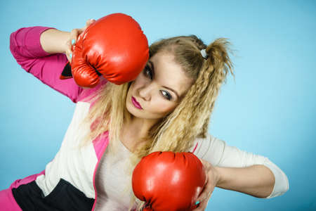 Sporty funny woman wearing red boxing gloves, trying to fight. Studio shot on blue background.の写真素材