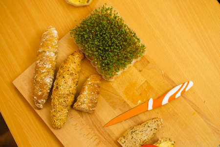 Baguette, knife and cuckooflower on wooden kitchen table, making delicious vegetarian sandwich.