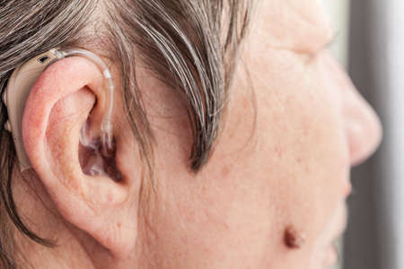Closeup senior woman with hearing aid in her ear. Health care, hear amplify, device for the deaf.