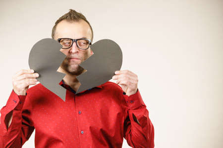 Depression, sadness, relationship problem concept. Man with broken heart full of negative sad emotions. Adult male holding two black halves of love symbol, on greyの写真素材