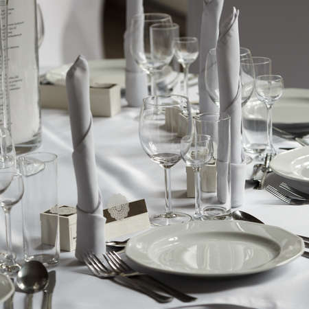 Detailed closeup of white tableware, cuttlery and wedding decorations on table. Bridal decor...