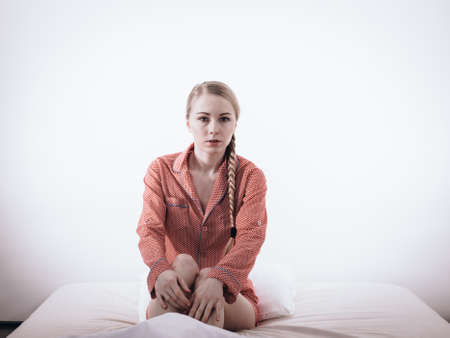 Adolescence problems concept. Sad young teenager woman sitting on bed feeling depressed.の写真素材
