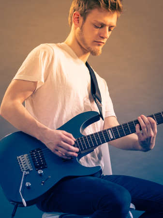 Young bearded man with electric guitar. Adult person is holding instrument and playing. Hobby, music concept, on greyの写真素材