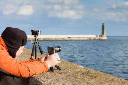 Man having leisure time walking on coastline during autumnal weather taking pictures using cameraの写真素材