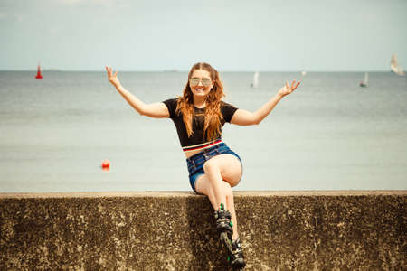 Happy joyful young woman wearing roller skates relaxing after long ride. Female being sporty having fun during summer time near sea.の写真素材
