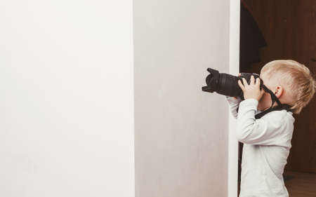 Child passion and hobbies concept. Kid playing with big professional digital camera, photographing various things in houseの写真素材