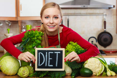 Young woman in kitchen having many green vegetables presenting board with diet sign.の写真素材