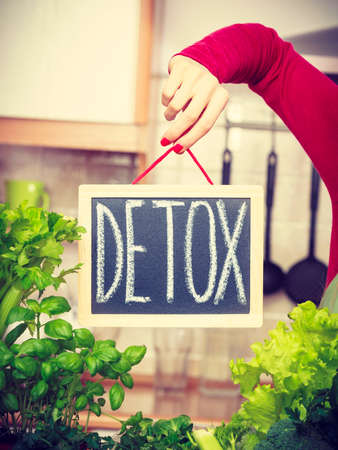 Young woman in kitchen having many green vegetables presenting board with detox sign.の写真素材
