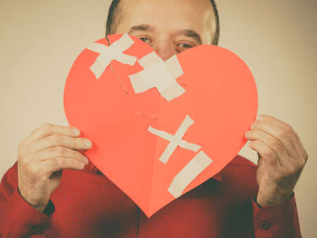 Bad relationships, breaking up, sadness emotions concept. Adult man holding broken heart, covering his face, on greyの写真素材