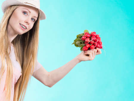 Happy cheerful teenage young woman ready for summer wearing pink outfit and sun hat holding delicious radishの写真素材