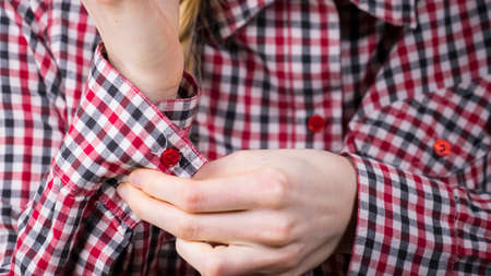 Woman rolling up the sleeves in checked shirt preparing before going out. Grey background.
