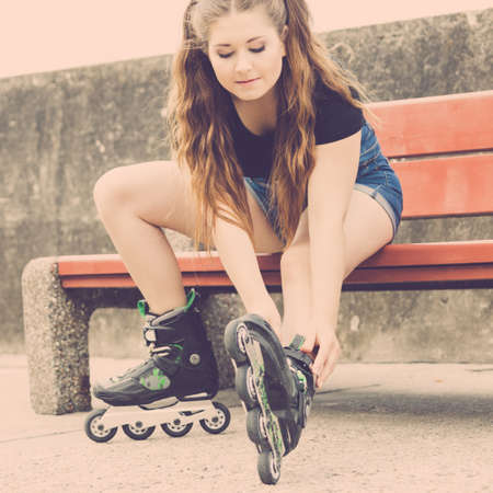 Young woman wearing roller skates outdoor. Fashionable fit girl having fun resting on bench.の写真素材