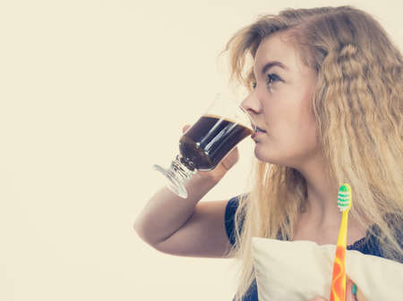 Funny woman holding black coffee and toothbrush being late. Getting morning energy, hurry up before going to work.の写真素材