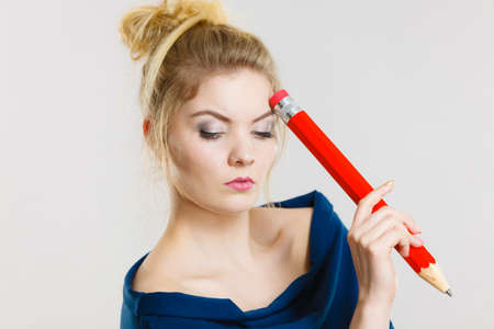 Student looking woman wearing nerdy eyeglasses holding big oversized pencil thinking about something.の写真素材