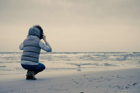 Relaxation and leisure. Woman walking on beach. Female tourist relax near to water place on nature. Autumn cold season.の写真素材