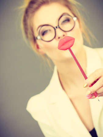 Happy elegant woman holding carnival accessoies on stick having fun at work wearing white office jacketの写真素材