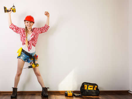 Woman wearing helmet using drill. Girl working at flat remodeling. Building, repair and renovation.の写真素材