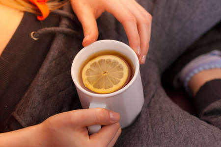 Woman hand holding cup of tea drink with lemon slice, view from top.の写真素材