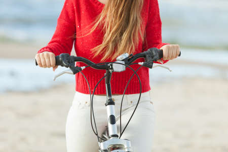 Unrecognizable woman bike cycling on sandy beach. Summer time sport recreation concept.