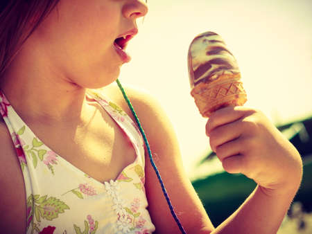 Summertime joy, summer recreation outside concept. Toddler girl in eyeglasses eating ice cream on...