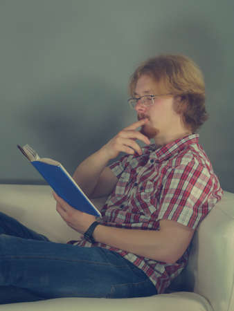 Man enjoying his leisure time relaxing while reading interesting book sitting on sofa. Relaxation...