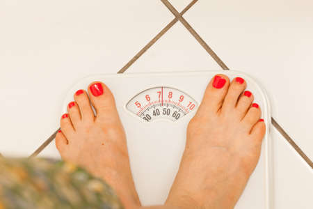 Woman feet standing on weight machine weighing scale showing results of dieting.