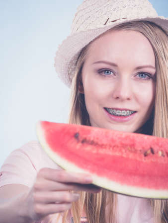 Happy cheerful teenage girl ready for summer wearing sun hat holding sweet fruit red juicy watermelon, on blueの写真素材