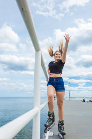 Happy joyful young woman wearing roller skates on sea. Girl having fun during summer time.