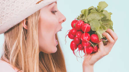 Funny young woman about to bite red delicious radish. Summer vegetables concept.の写真素材