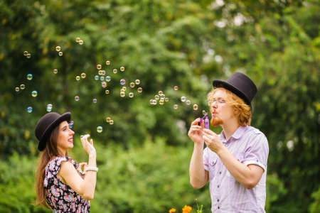 Happiness and carefree concept. Young woman and man having fun blowing soap bubbles together outdoor in parkの写真素材