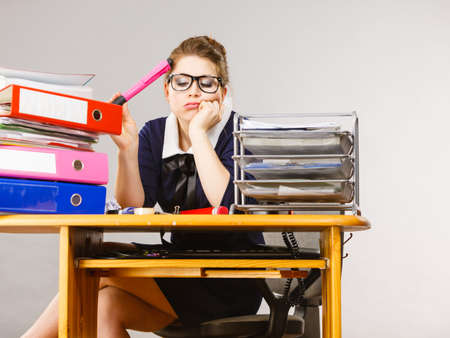 Sleepy business woman doing her work sitting working at desk full off documents in binders being bored or tired staying up late.の写真素材