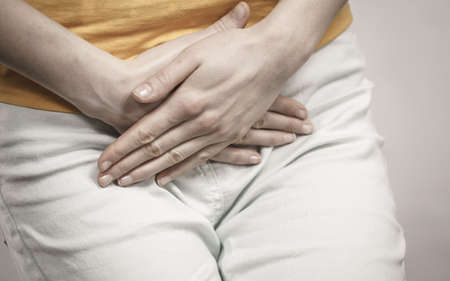 Closeup young sick woman with hands holding pressing her crotch lower abdomen. Medical or...