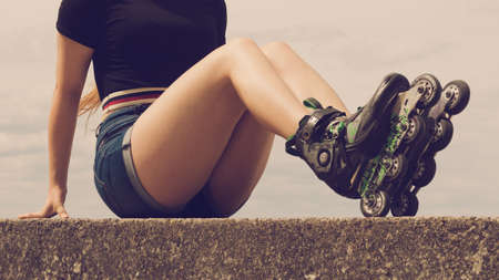Sexy woman slim legs wearing roller skates sitting outside. Sport activity concept.