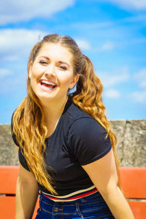 Happy teen woman enjoying her leisure time. Female having long brown hair posing with sky in...