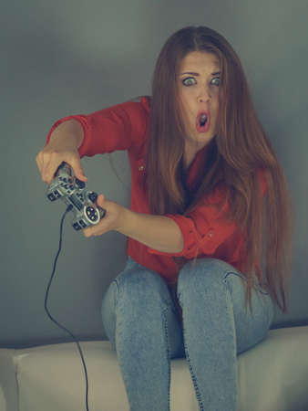 Nerd geek shocked adult women playing on the video console holding game pad sitting on sofa. Gaming...