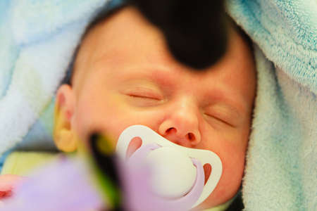 Little newborn baby in pyjamas lying on back and sleeping in bedding, dummy in mouth. Family, parenthood, childhood concept.の写真素材